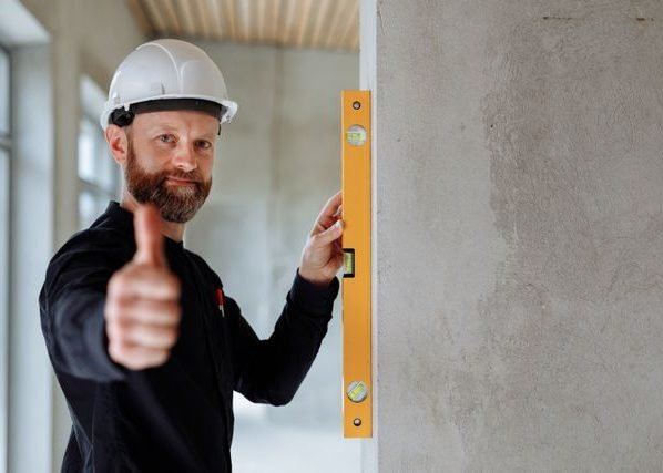 A builder in a hard hat checking a wall with a yellow spirit level